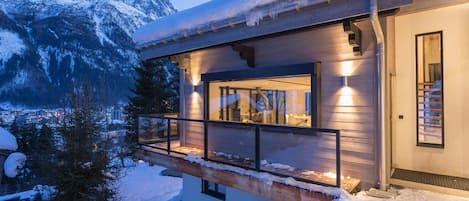 A modern chalet with a balcony overlooking a snowy landscape and mountains.