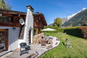 Eine Holzchalet mit Steinkamin, Grill und einer Terrasse mit Gartenmöbeln.