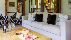 A cozy living room with a sofa, wooden beams, a coffee table with food and wine glasses, and a staircase.