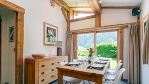 A dining area with a wooden table set for four, white chairs, a wooden cabinet, and a window with curtains.