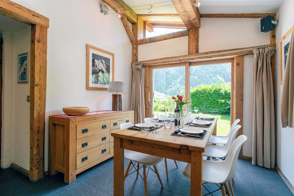 Un coin repas avec une table en bois dressée pour quatre personnes, un buffet en bois et une fenêtre agrémentée de rideaux.