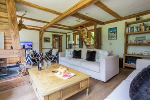 Ein rustikaler Innenraum mit freiliegenden Holzbalken, einem weißen Sofa, einem Couchtisch mit Speisen und einem Bücherregal mit Büchern und Dekoration.