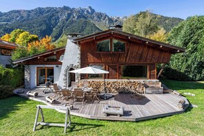 Een houten chalet met terras, buitenzitplaatsen en een berg op de achtergrond.