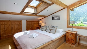 A bedroom with a wooden bed, a skylight, a mountain view, and a small wooden nightstand.