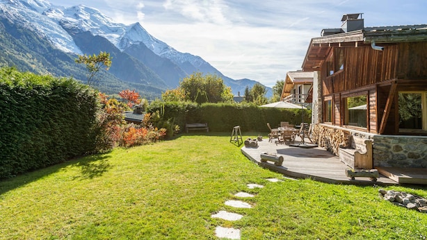 A wooden house with a stone foundation, a deck, and a view of snow-capped mountains.