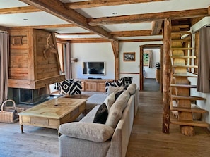 Een rustiek interieur met een houten plafond, een open haard, een bank, een televisie en een trap.