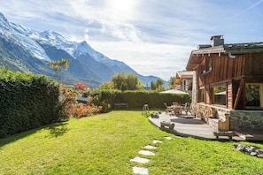 Une cabane en bois, construite sur des fondations en pierre, entourée d’une pelouse bien entretenue et d’un mur de pierres.