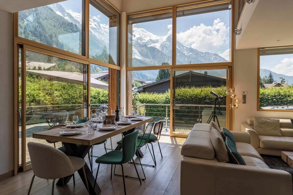 A spacious room with large windows offering mountain views, a dining area with a table set for four, and a comfortable seating area with a sofa.
