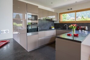 A modern kitchen with stainless steel appliances, a large window, and a view of greenery outside.