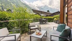 A deck with outdoor furniture, a table with a bottle and glasses, and a view of mountains. - Chalet Couttet -  a self catered chalet that sleeps 8 guests  in 4 bedrooms (Chamonix)