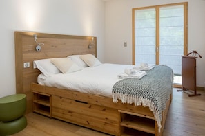 A bedroom with a wooden bed frame, a green stool, and a window with a view.