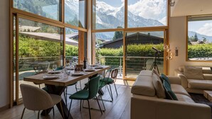 A dining area with a table set for four, large windows with mountain views, and a sofa in the foreground. - Chalet Couttet -  a self catered chalet that sleeps 8 guests  in 4 bedrooms (Chamonix)