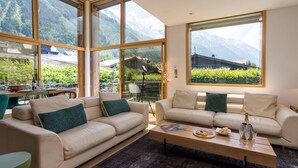 A modern living room with two beige sofas, a wooden coffee table, and large windows offering mountain views. - Chalet Couttet -  a self catered chalet that sleeps 8 guests  in 4 bedrooms (Chamonix)