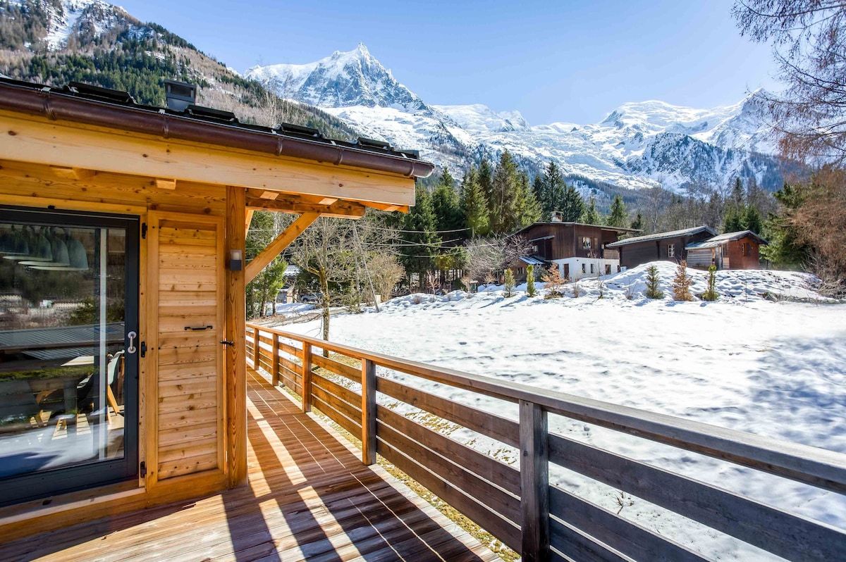 Eine Holzhütte mit einer Terrasse mit Blick auf eine verschneite Landschaft und Berge.