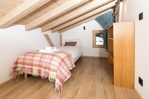 A bedroom with a wooden ceiling, a bed with a plaid blanket, a window with a view of snow, and a wooden wardrobe. - Chalet de l'Ours, Mt Blanc views, Chamonix All Year (Chamonix)