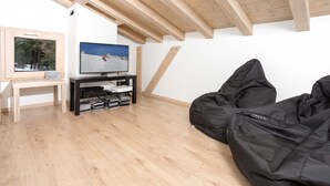Een moderne woonkamer met een houten plafond, een flatscreen-tv, een zwarte loungestoel en een klein houten tafeltje met boeken.