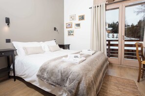 A hotel room with a bed, a nightstand, a desk, a chair, a window with a view of a snowy landscape, and a wall with framed pictures.