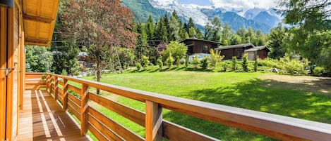 Una terraza de madera con vistas a un paisaje montañoso y una cabaña pequeña.