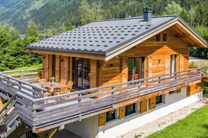A wooden cabin with a balcony, large windows, and a mountain backdrop.