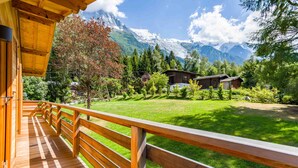 Een houten terras met houten balustrade, met uitzicht op een gazon met bomen en een berg op de achtergrond.