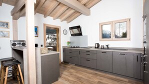 Een moderne keuken met houten balken, grijze kasten, een geïntegreerd eiland, barkrukken, een radio en een raam met uitzicht op de bergen.