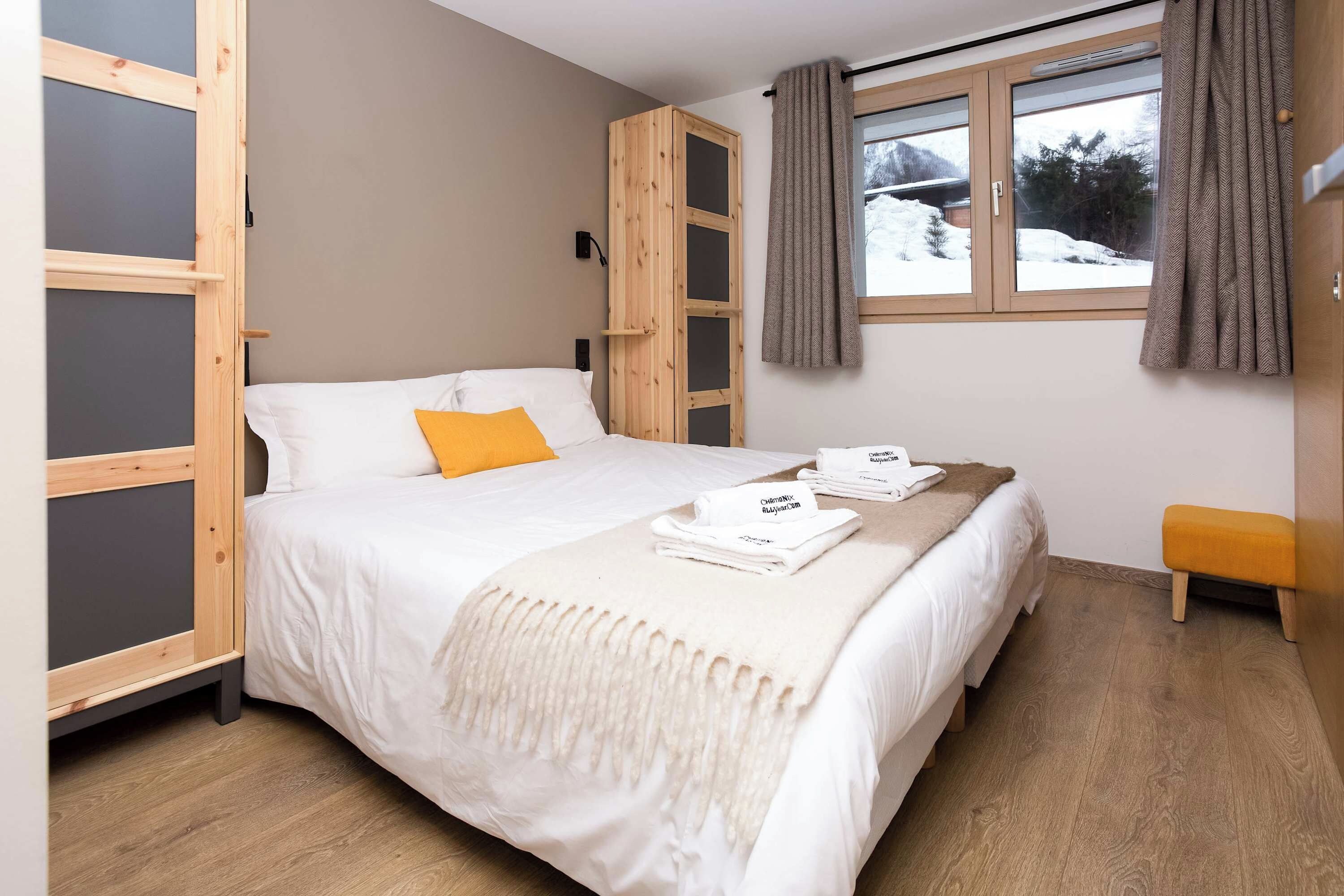 Un dormitorio con una cama, una ventana con cortinas y un pequeño banco.