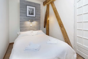 A bedroom with a bed, a framed picture on the wall, and a wooden ceiling beam.