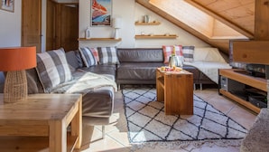 A cozy loft bedroom with a sloped ceiling, a large bed, a wooden TV stand, and a seating area with a sofa and a coffee table.