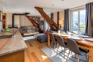 Eine moderne Küche mit einer Granit-Arbeitsplatte, ein Essbereich mit einem Holztisch für vier Personen und ein gemütlicher Wohnbereich mit einer Couch und Bücherregalen.