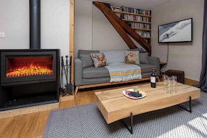 Een gezellige woonkamer met een open haard, een bank met decoratieve kussens, een boekenkast en een aan de muur bevestigde televisie.