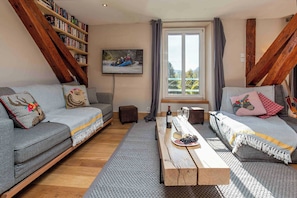 A cozy living room with two grey sofas, a wooden coffee table, a bookshelf, and a window with curtains.