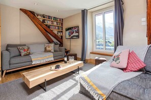 Ein Wohnzimmer mit einer Couch, einem Couchtisch mit einer Flasche und Gläsern, einem Bücherregal, einem Gemälde und einem Fenster mit Blick.