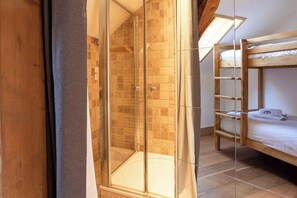Ein Zimmer mit einer gläsernen Dusche, einem Stockbett und einer Holzlade.
