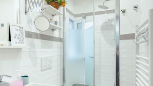 Une salle de bain moderne avec une douche à parois de verre, des carreaux blancs, un lavabo blanc et un miroir.
