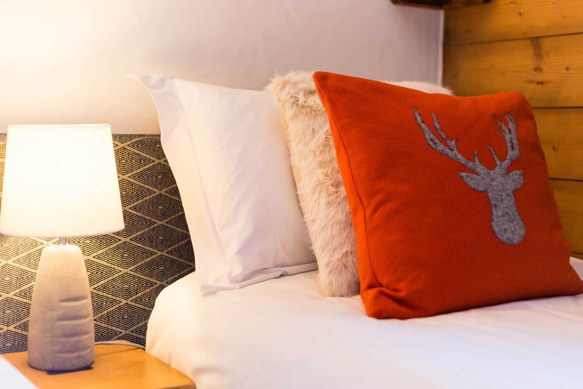 A bed with white bedding, a red pillow with a deer design, a white pillow, and a patterned wall.
