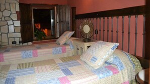 A bedroom with two beds, a stone wall, a wooden door, and a metal railing.