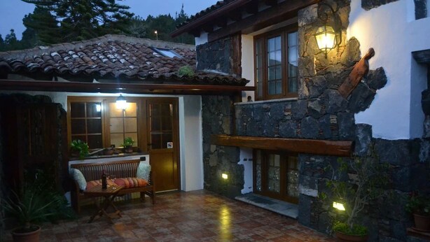 A stone building with a tiled roof, a wooden bench, and potted plants.