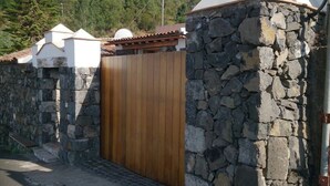 A stone wall with a wooden gate, a white building with a tiled roof, and a satellite dish.