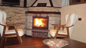 A cozy living room with a stone fireplace, two wooden chairs, and a television mounted on the wall.