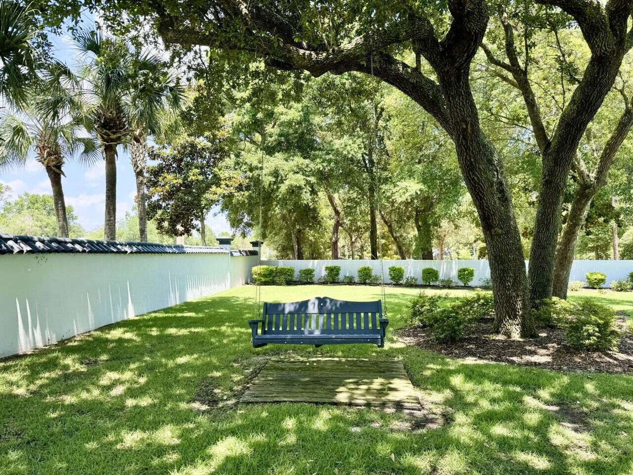 Un parc amb una banca sota un arbre gran, envoltat de gespa ben cuidada i una tanca blanca.