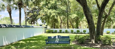 Un parc amb una banca sota un arbre gran, envoltat de gespa ben cuidada i una tanca blanca.