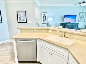 A kitchen with a dishwasher, two sinks, a television, and framed artwork on the wall.