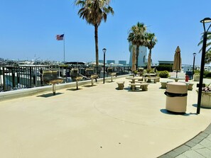A waterfront promenade with benches, a trash can, and a flag.
