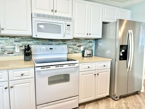 A modern kitchen with white cabinetry, a stainless steel refrigerator, a microwave, an oven, and a toaster.