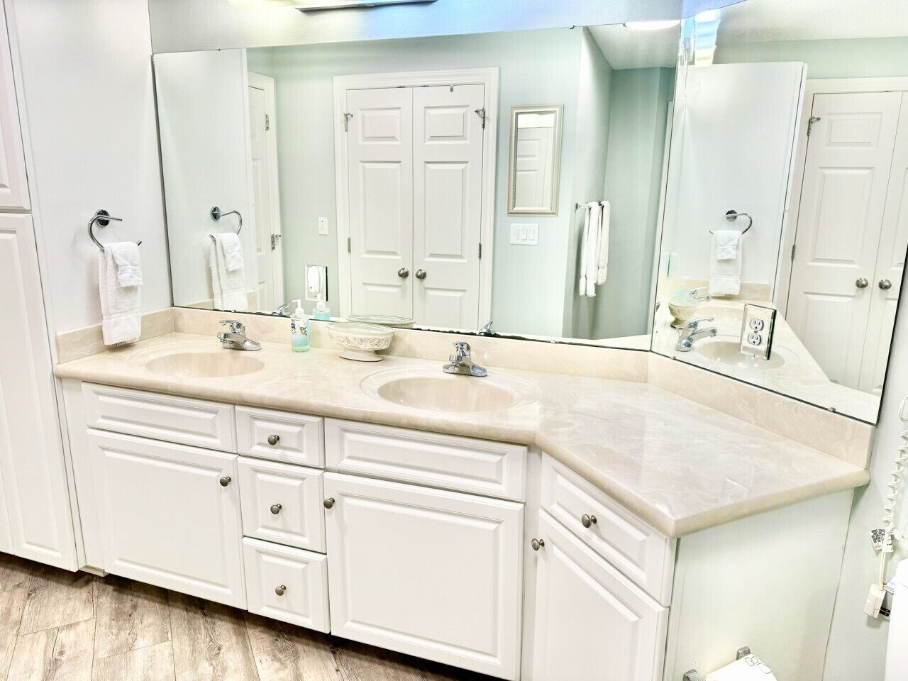 A bathroom with two sinks, a large mirror, and white cabinetry.