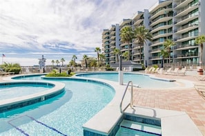 Un hotel con una grande piscina esterna, diversi balconi e palme.