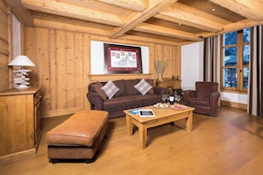 Un salon chaleureux avec un plafond en bois, un canapé en cuir marron, un fauteuil en cuir marron, une table basse en bois et un tableau encadré accroché au mur.