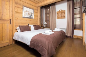 A wooden-paneled room with a bed, a painting, a window with curtains, and a wooden cabinet. - Le Kursaal Apartment, Ski/Hike, Chamonix All Year (Chamonix)