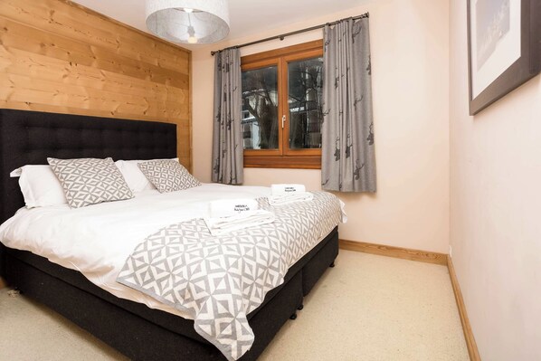 A bedroom with a bed, pillows, a window with curtains, and a headboard.