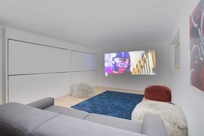 A modern living room with a grey sofa, a blue rug, and a flat-screen TV mounted on the wall.